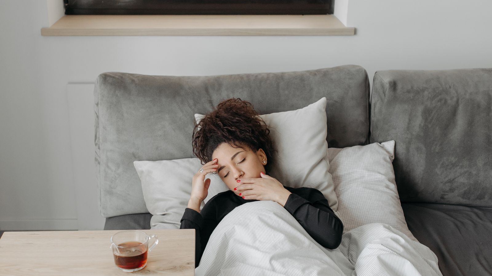 Woman resting in bed with warm tea, showing the prolonged fatigue that follows dengue fever recovery